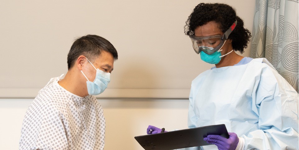 health care worker in a protective respirator and goggles conversing with patient
